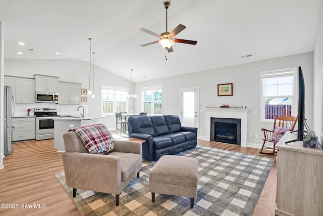 living room featuring lofted ceiling, sink, ceiling fan with notable chandelier, and light wood-type flooring