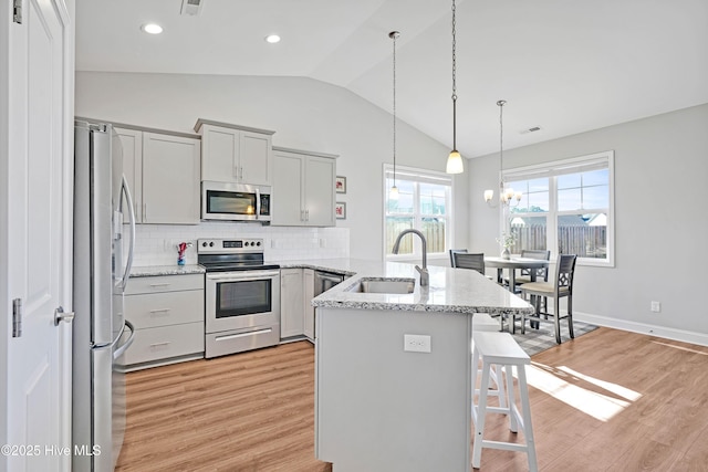 kitchen with a breakfast bar, sink, tasteful backsplash, appliances with stainless steel finishes, and light stone countertops