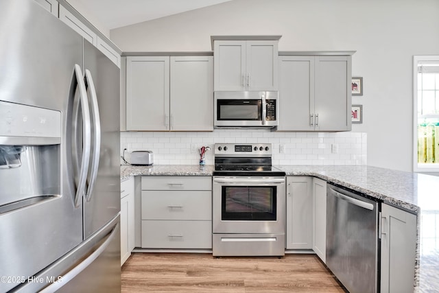 kitchen with vaulted ceiling, tasteful backsplash, kitchen peninsula, stainless steel appliances, and light stone countertops