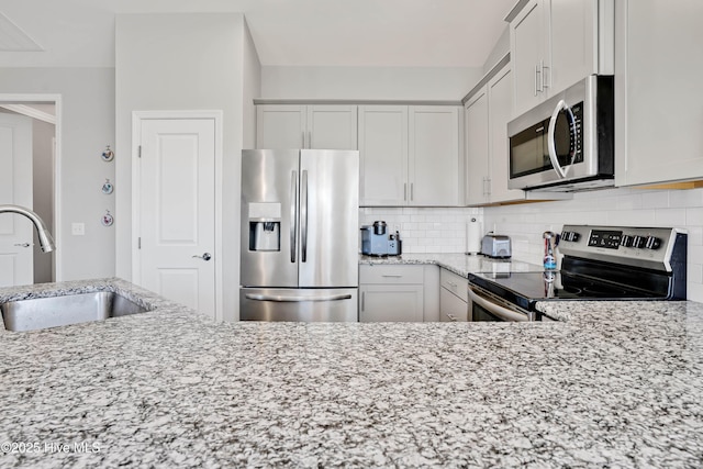 kitchen featuring sink, appliances with stainless steel finishes, light stone countertops, white cabinets, and decorative backsplash