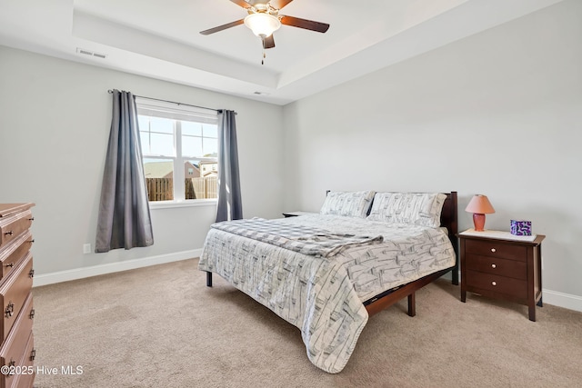 bedroom with light colored carpet, ceiling fan, and a tray ceiling