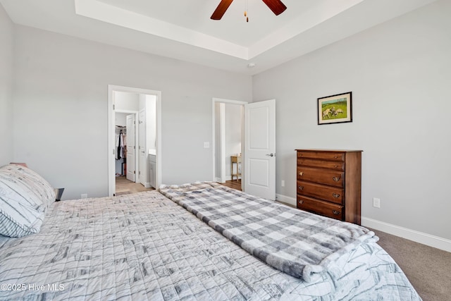 bedroom featuring ceiling fan, ensuite bathroom, a raised ceiling, and light carpet