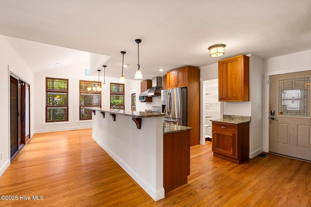 kitchen with wall chimney range hood, hanging light fixtures, light hardwood / wood-style floors, a kitchen bar, and stainless steel fridge with ice dispenser