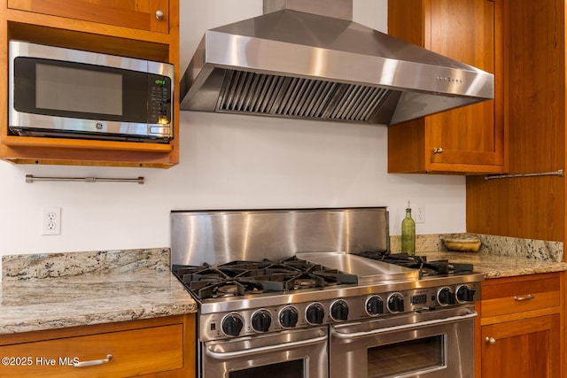 kitchen featuring light stone counters, wall chimney exhaust hood, and appliances with stainless steel finishes