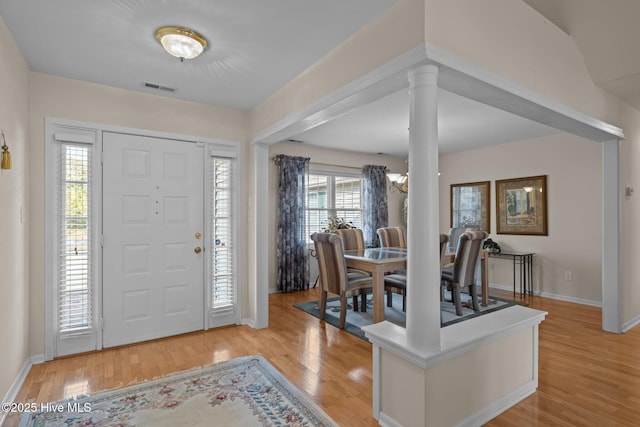 foyer entrance with a notable chandelier, light hardwood / wood-style floors, and decorative columns