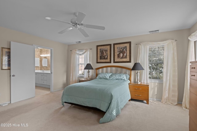 bedroom with connected bathroom, light colored carpet, and ceiling fan