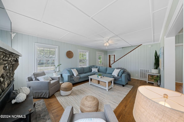 living room featuring hardwood / wood-style floors, a fireplace, wooden walls, and ceiling fan