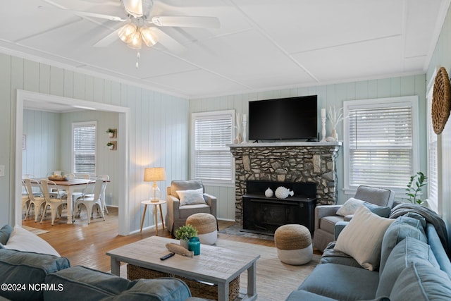 living room with ceiling fan, a healthy amount of sunlight, a stone fireplace, and light hardwood / wood-style floors