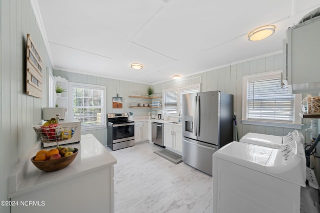 kitchen with wood walls, white cabinetry, ornamental molding, stainless steel appliances, and washing machine and dryer