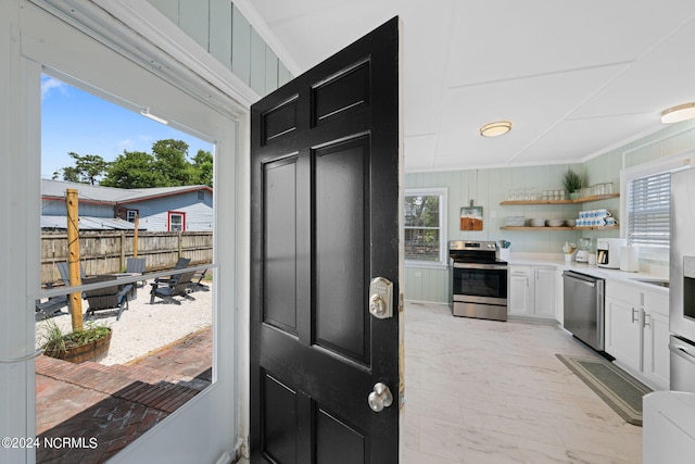 kitchen with crown molding, appliances with stainless steel finishes, white cabinets, and wooden walls