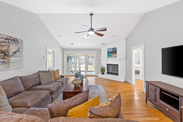 living room featuring ceiling fan, a brick fireplace, high vaulted ceiling, and light wood-type flooring