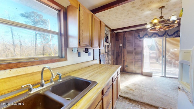 kitchen featuring sink, wooden counters, light carpet, hanging light fixtures, and a wealth of natural light