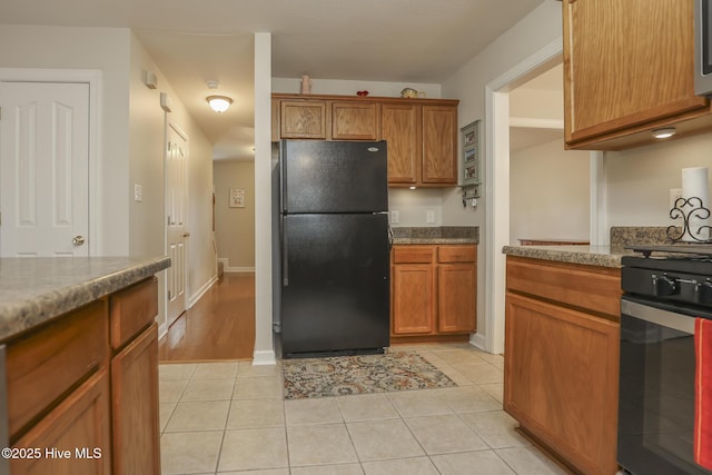 kitchen with light tile patterned flooring, baseboards, range, freestanding refrigerator, and brown cabinetry