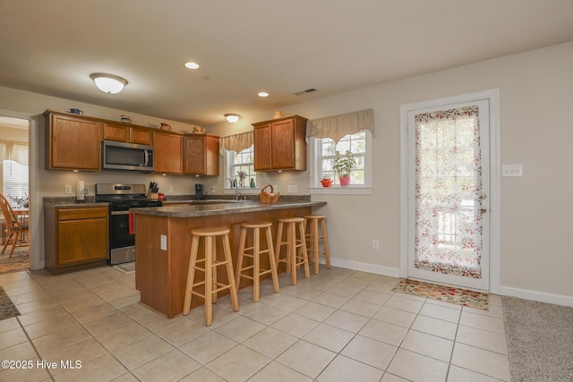 kitchen featuring appliances with stainless steel finishes, dark countertops, brown cabinetry, and a peninsula