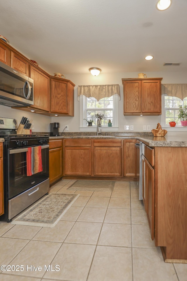 kitchen with stainless steel appliances, a wealth of natural light, brown cabinets, and light tile patterned floors