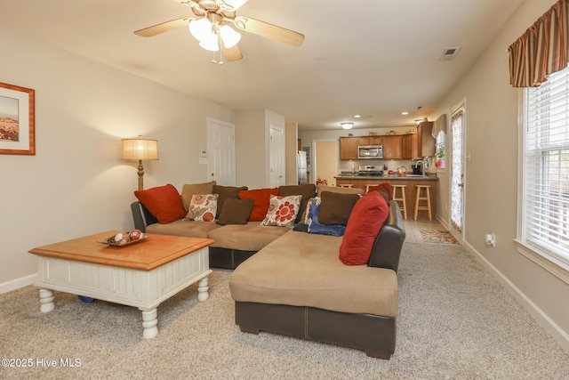 living area with a ceiling fan, light colored carpet, visible vents, and baseboards