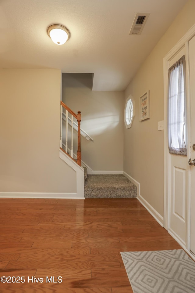 foyer entrance with stairs, wood finished floors, visible vents, and baseboards