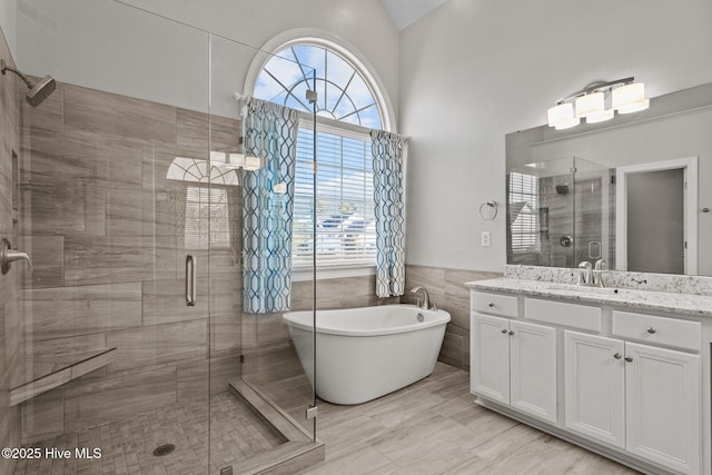 bathroom with tile walls, vanity, vaulted ceiling, and plus walk in shower