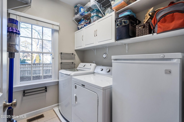 clothes washing area with cabinets, washing machine and clothes dryer, and light tile patterned flooring