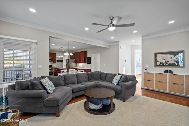 living room with wood-type flooring, ornamental molding, and ceiling fan with notable chandelier