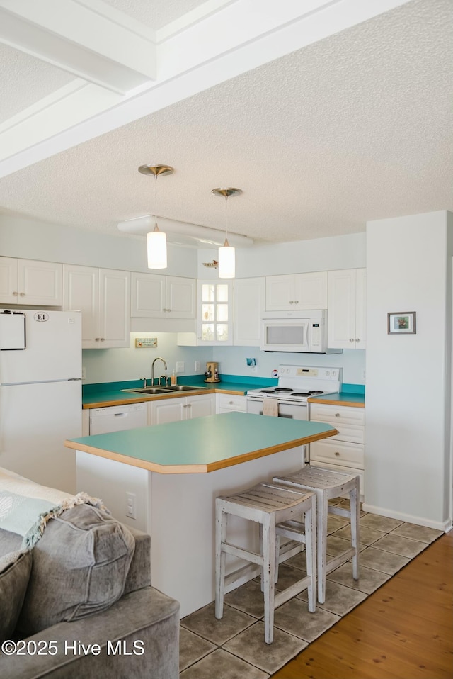 kitchen featuring hanging light fixtures, white appliances, a center island, and white cabinets