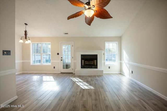 unfurnished living room with wood-type flooring, a brick fireplace, a healthy amount of sunlight, and ceiling fan with notable chandelier