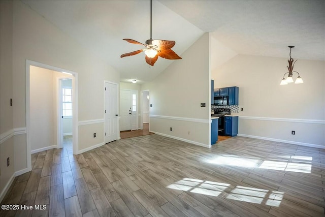 unfurnished living room with high vaulted ceiling, ceiling fan with notable chandelier, and light wood-type flooring