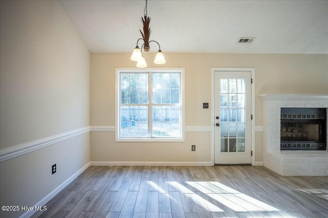 doorway featuring an inviting chandelier, hardwood / wood-style floors, and a brick fireplace