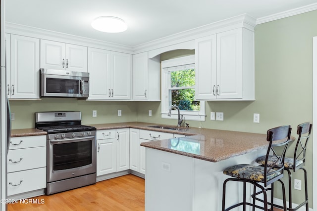 kitchen with sink, a breakfast bar area, appliances with stainless steel finishes, kitchen peninsula, and white cabinets