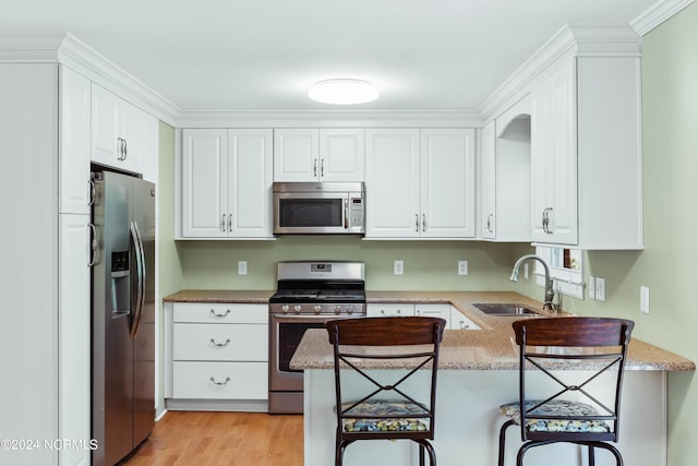 kitchen featuring sink, stainless steel appliances, white cabinets, a kitchen bar, and kitchen peninsula