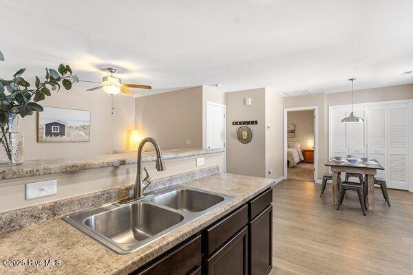 kitchen with sink, dark brown cabinets, hanging light fixtures, light wood-type flooring, and ceiling fan