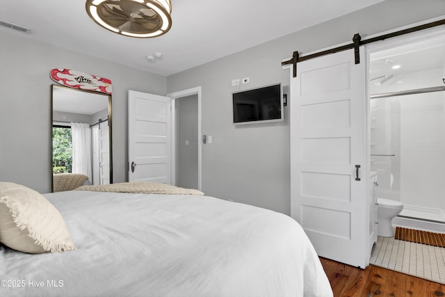 bedroom featuring ensuite bathroom, a barn door, and dark wood-type flooring