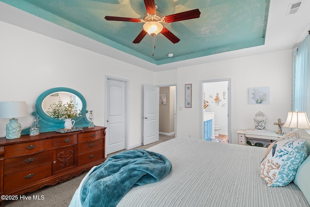 bedroom with a raised ceiling, ceiling fan, light colored carpet, and ensuite bath