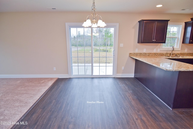 kitchen with sink, hanging light fixtures, dark brown cabinets, kitchen peninsula, and light stone countertops