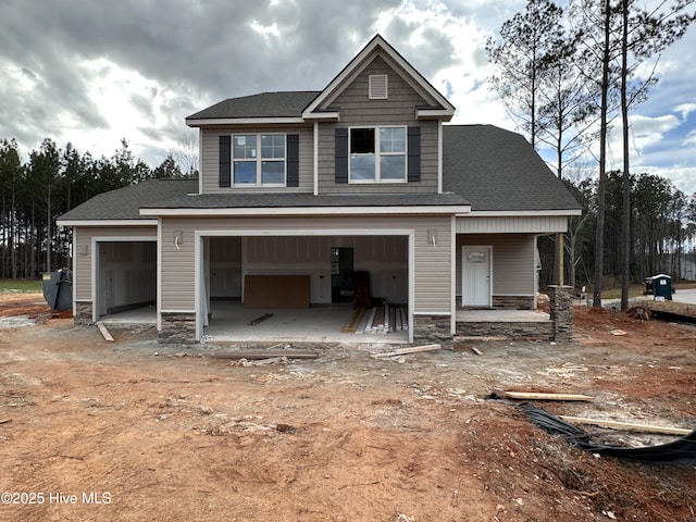 view of front facade with an attached garage, stone siding, dirt driveway, and roof with shingles