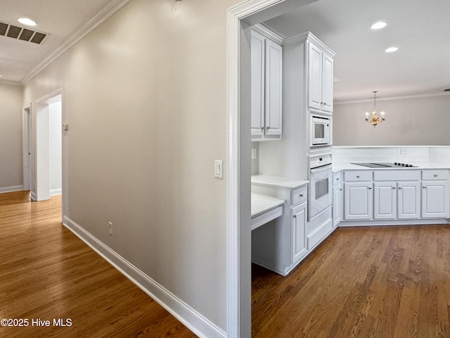 interior space with white cabinetry, an inviting chandelier, crown molding, white appliances, and hardwood / wood-style floors