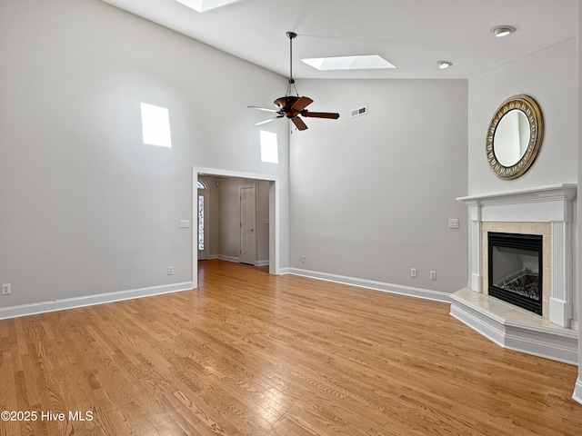 unfurnished living room with a skylight, high vaulted ceiling, light hardwood / wood-style flooring, a tile fireplace, and ceiling fan