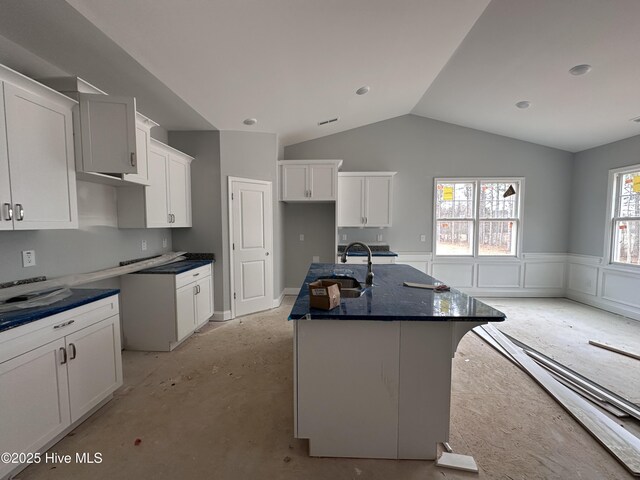 kitchen featuring dark countertops, wainscoting, a kitchen island, vaulted ceiling, and white cabinetry