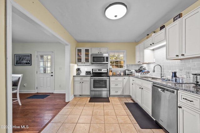 kitchen with sink, dark stone countertops, white cabinets, backsplash, and stainless steel appliances