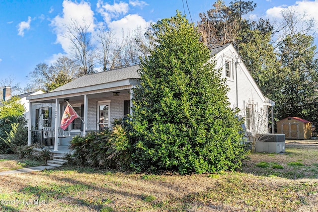 view of front facade featuring a front lawn, central air condition unit, covered porch, and a storage shed