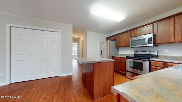 kitchen featuring crown molding, appliances with stainless steel finishes, a center island, and light hardwood / wood-style flooring