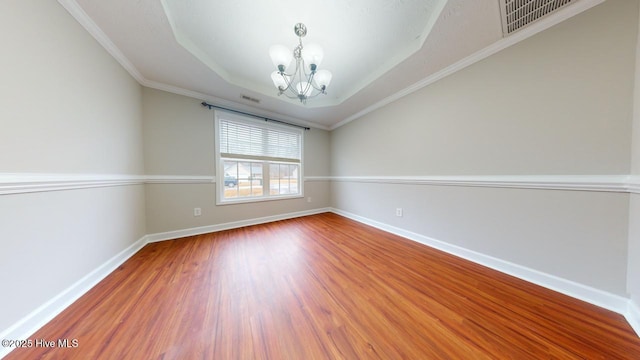 unfurnished room featuring an inviting chandelier, a tray ceiling, ornamental molding, and hardwood / wood-style flooring