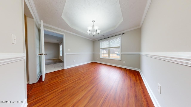 interior space with wood-type flooring, a chandelier, a raised ceiling, crown molding, and a textured ceiling