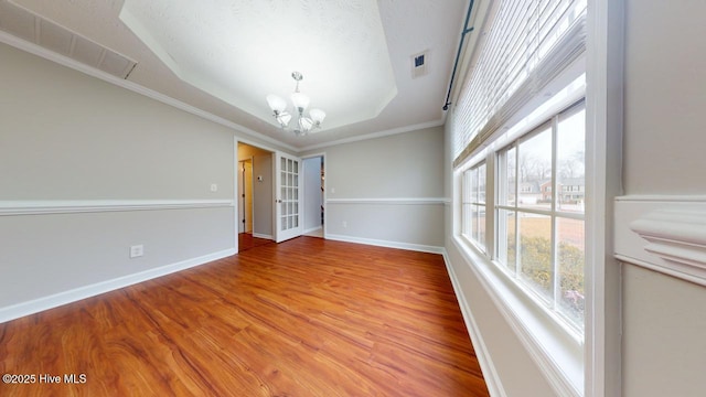 empty room with hardwood / wood-style flooring, crown molding, a chandelier, and a tray ceiling