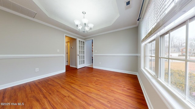 spare room with crown molding, wood-type flooring, a raised ceiling, and a chandelier