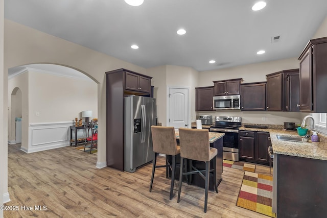 kitchen with a breakfast bar, sink, light stone counters, a center island, and appliances with stainless steel finishes