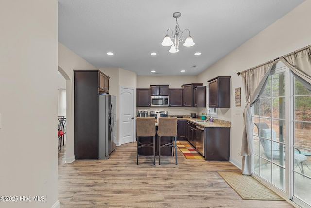 kitchen featuring a center island, hanging light fixtures, dark brown cabinets, stainless steel appliances, and light hardwood / wood-style floors