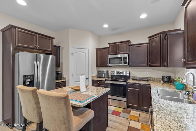 kitchen with sink, a breakfast bar area, light stone counters, light hardwood / wood-style flooring, and appliances with stainless steel finishes