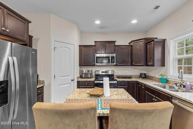 kitchen with sink, a breakfast bar, appliances with stainless steel finishes, dark brown cabinets, and light stone counters