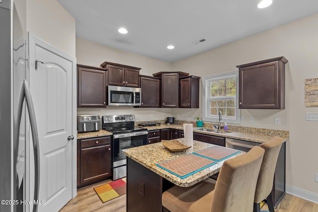 kitchen featuring sink, stainless steel appliances, a kitchen breakfast bar, dark brown cabinetry, and light wood-type flooring